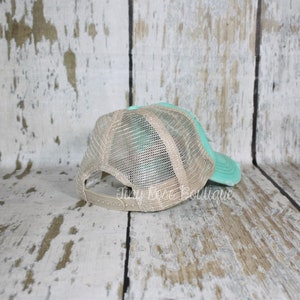 Pu&ograve; includere: Un cappello da camionista in rete color turchese e beige con cinturino regolabile marrone. Il cappello &egrave; mostrato dal retro.