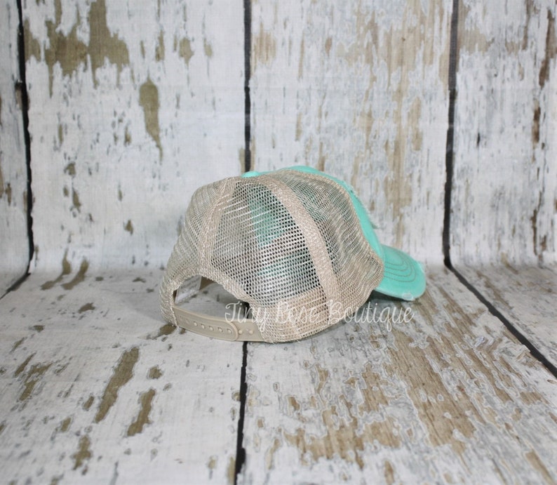 Pu&ograve; includere: Un cappello da camionista in rete color turchese e beige con cinturino regolabile marrone. Il cappello &egrave; mostrato dal retro.