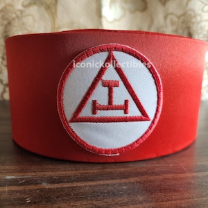May include: Red Masonic hat with a white embroidered emblem featuring a triangle with a letter 'I' and a horizontal line with two vertical lines.