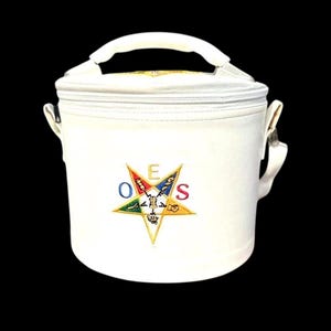 Puede incluir: Bolsa de almuerzo aislante blanca con cierre de cremallera, asa superior y correa para el hombro. La bolsa presenta un emblema bordado con las letras OES y un diseño de estrella en varios colores. La bolsa está diseñada para mantener fríos los alimentos y bebidas.