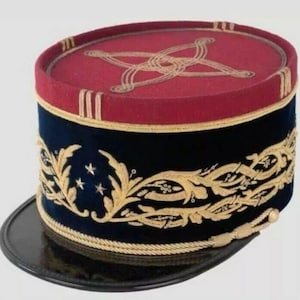Op de afbeelding: Een vintage militaire hoed met een zwarte rand en een cilindrische kroon. De kroon is marineblauw met goud geborduurde bladeren en drie sterren. De bovenkant is bordeauxrood met gouden borduursel.