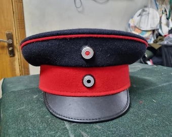 May include: A black and red military style hat with a black leather band and two silver buttons with white centers.