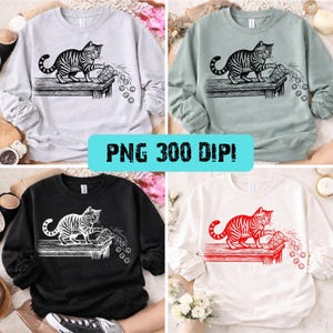 以下が含まれることがあります： ライトグレー、セージグリーン、ブラック、ホワイトの4色のスウェットシャツ。それぞれ、テーブルから物をこぼしているトラ猫のグラフィックが特徴です。「PNG 300 DPI！」の文字がターコイズ色の長方形に入っています。