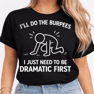 Puede incluir: Camiseta negra con texto blanco y un gráfico de una persona haciendo un burpee. El texto dice: "I'll do the burpees, I just need to be dramatic first."