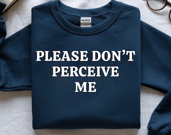 May include: Navy blue sweatshirt with the text "PLEASE DON'T PERCEIVE ME" in white block letters. The sweatshirt is a crew neck style and appears to be made of a soft material. The Gildan brand label is visible.