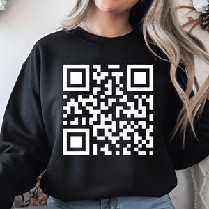 May include: Black sweatshirt featuring a large white QR code design. The QR code is a square matrix of black and white squares, creating a unique pattern. The sweatshirt is a solid black color.