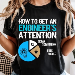 May include: Black t-shirt with the text "HOW TO GET AN ENGINEER'S ATTENTION" in white and teal. Below the text is a pie chart with the words "BREAK SOMETHING" and "FREE COFFEE". The chart has a light blue, white, and brown color scheme.