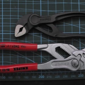 May include: Two pairs of pliers, one black and one silver, with red handles. The black pliers are labeled "KNIPEX" and the silver pliers are labeled "KNIPEX 86 03 150" and "CD SW27/1".