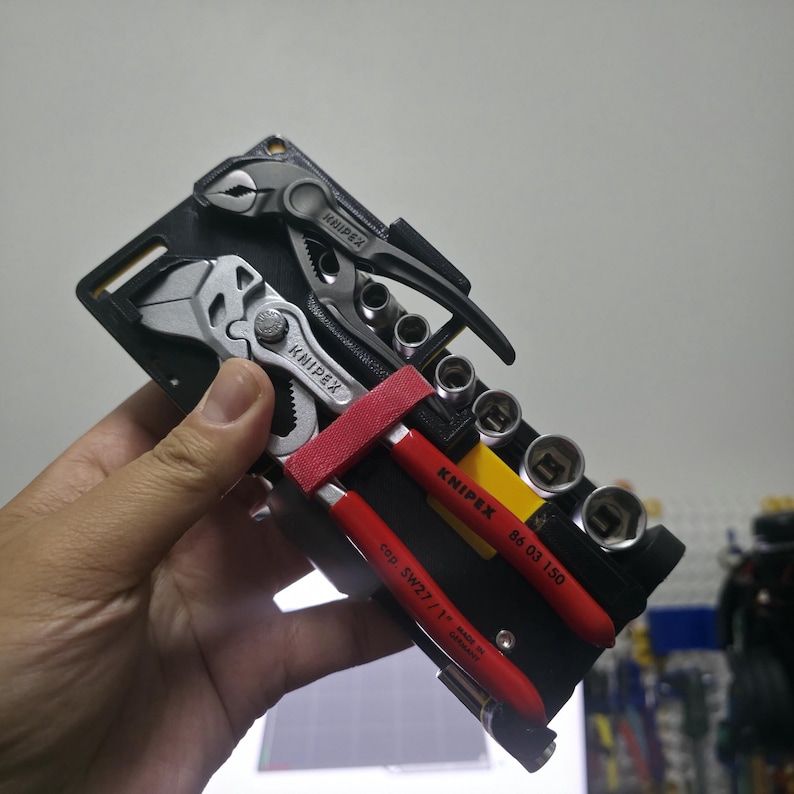 May include: A black multi-tool with a red strap, containing pliers, screwdrivers, and sockets. The tools are made by Knipex and are labeled with the brand name.