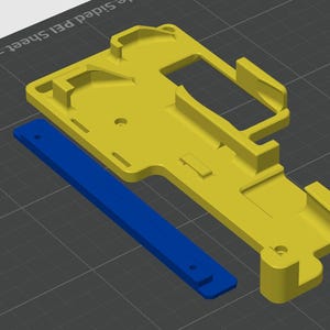 May include: A yellow 3D printed plastic part with a blue plastic strip attached to it. The part has a complex design with multiple holes and slots.