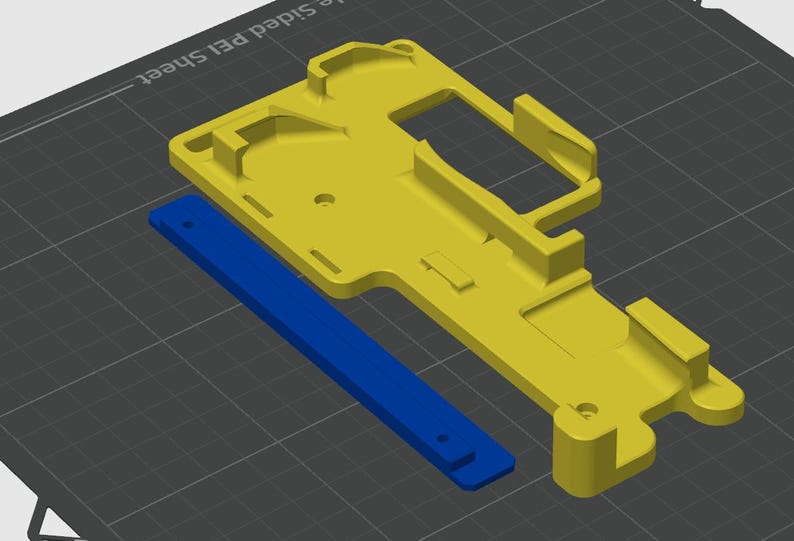 May include: A yellow 3D printed plastic part with a blue plastic strip attached to it. The part has a complex design with multiple holes and slots.
