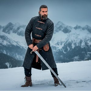 Könnte beinhalten: Ein schwarzer, gesteppter Mantel mit Lederriemen und einem braunen Ledergürtel. Der Mantel wird über einer schwarzen Hose und braunen Stiefeln getragen. Ein langes silbernes Schwert wird vor einem schneebedeckten Bergpanorama gehalten.