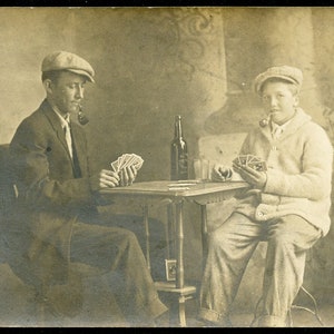 Pai e filho FUMANDO CACHIMBOS e BEBENDO CERVEJA enquanto jogam cartas - Cartão postal fotográfico de 1910