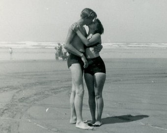 Jóvenes amantes COMPARTIENDO un BESO en la PLAYA de Long Beach, Washington en 1953 Foto instantánea