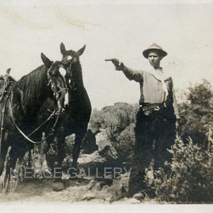KOWBOJ celuje swoim PISTOLETEM, podczas gdy KONIE patrzą na niego na oryginalnej pocztówce fotograficznej z lat 1910.