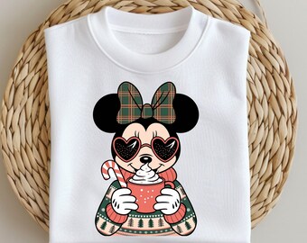 May include: White sweatshirt with a cartoon image of Minnie Mouse wearing heart-shaped sunglasses and a plaid bow. She is holding a red mug with a white swirl on top and a candy cane.
