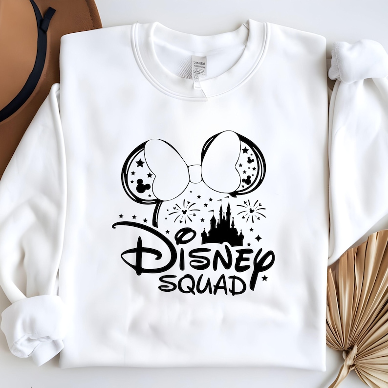Pu&ograve; includere: Felpa bianca con una grafica nera delle orecchie di Topolino con un fiocco, un castello, fuochi d'artificio e il testo "Disney Squad".