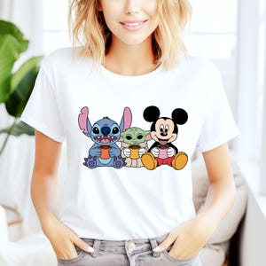 Puede incluir: Camiseta blanca con un estampado gr&aacute;fico de Stitch, Baby Yoda y Mickey Mouse sosteniendo tazas de caf&eacute;.