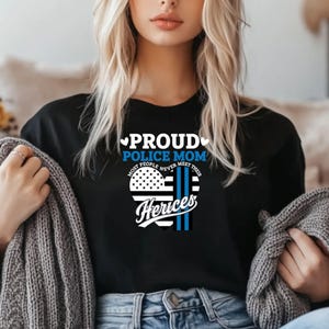 May include: Black t-shirt with a white heart design that says "Proud Police Mom" and "Most People Never Meet Their Heros".