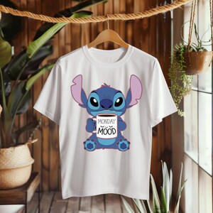 Puede incluir: Camiseta blanca con un personaje azul Stitch sosteniendo una taza de caf&eacute; que dice "Monday Mood".