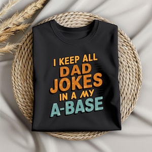 Könnte beinhalten: Schwarzes T-Shirt mit einer bunten Grafik, auf der "I keep all dad jokes in a my a-base" steht.