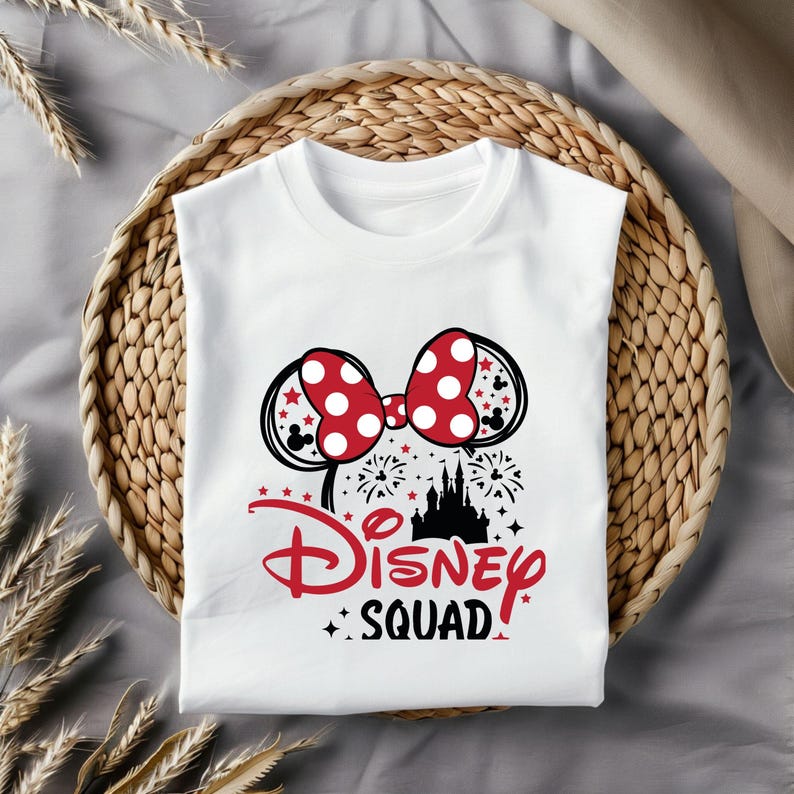 Pu&ograve; includere: Maglietta bianca con una grafica nera e rossa delle orecchie di Topolino con un fiocco rosso e pois bianchi. La grafica include anche una silhouette nera del castello di Cenerentola con fuochi d'artificio e il testo "Disney Squad".
