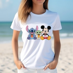 Puede incluir: Camiseta blanca con un gr&aacute;fico de Stitch, Baby Yoda y Mickey Mouse sosteniendo tazas de caf&eacute;.