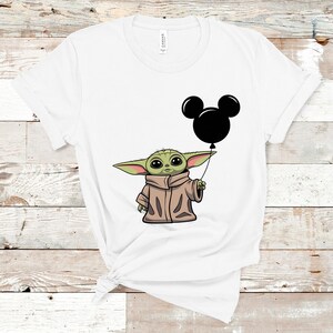 K&ouml;nnte beinhalten: Wei&szlig;es T-Shirt mit einer gr&uuml;nen Figur, die einen schwarzen Mickey Mouse-Ballon h&auml;lt.