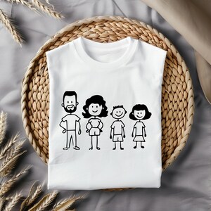 May include: White t-shirt featuring a black line drawing of a family of four. The illustration depicts a man with a beard, a woman, and two children. The shirt is displayed on a woven basket.