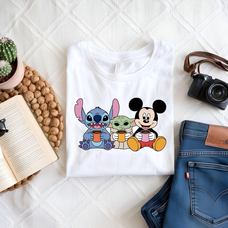 Puede incluir: Camiseta blanca con un gr&aacute;fico de Stitch, Baby Yoda y Mickey Mouse sosteniendo tazas de caf&eacute;.