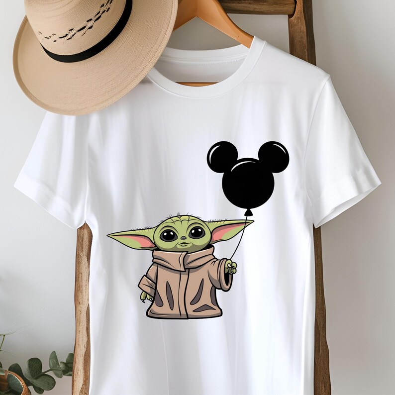 K&ouml;nnte beinhalten: Wei&szlig;es T-Shirt mit einer gr&uuml;nen Figur, die einen schwarzen Mickey Mouse-Ballon h&auml;lt.