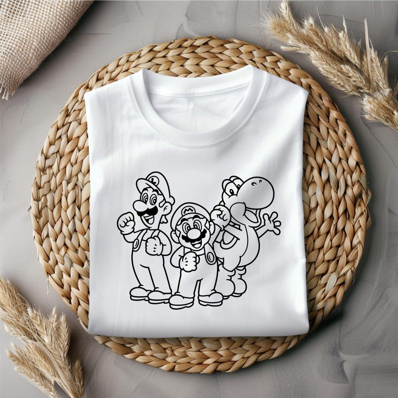 May include: White t-shirt featuring a black and white graphic of Mario, Luigi, and Yoshi. The characters are standing side by side. The t-shirt is folded on a woven, circular placemat.