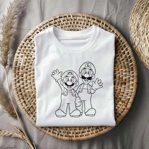 May include: White t-shirt featuring a black outline illustration of two cartoon characters, one with an "M" on their hat and the other with an "L". Both characters are waving. The shirt is displayed on a woven basket.