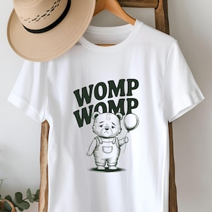 May include: White t-shirt with a black and white illustration of a bear holding a balloon. The text "WOMP WOMP" is printed in green above the bear.