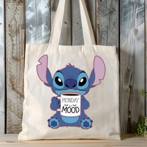 Puede incluir: Una bolsa de tela blanca con un personaje azul Stitch sosteniendo una taza de caf&eacute; que dice "Monday Mood".