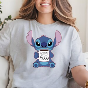 Puede incluir: Una camiseta gris claro con un personaje azul Stitch sosteniendo una taza de caf&eacute; que dice "Monday Mood".