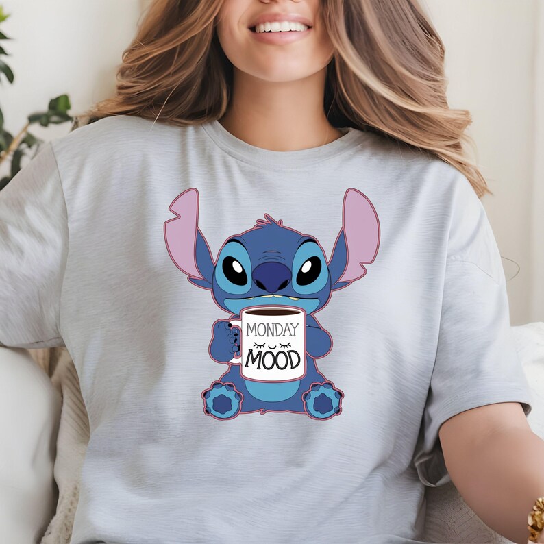 Puede incluir: Una camiseta gris claro con un personaje azul Stitch sosteniendo una taza de caf&eacute; que dice "Monday Mood".