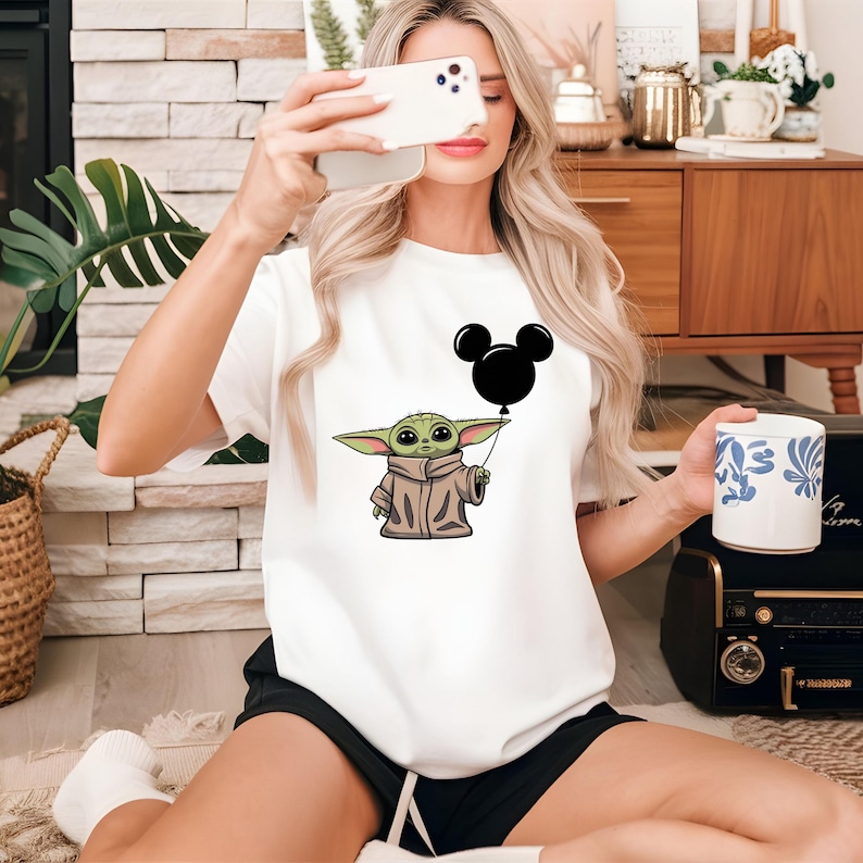 K&ouml;nnte beinhalten: Wei&szlig;es T-Shirt mit einer gr&uuml;nen Comicfigur, die einen schwarzen Mickey-Maus-Ballon h&auml;lt.