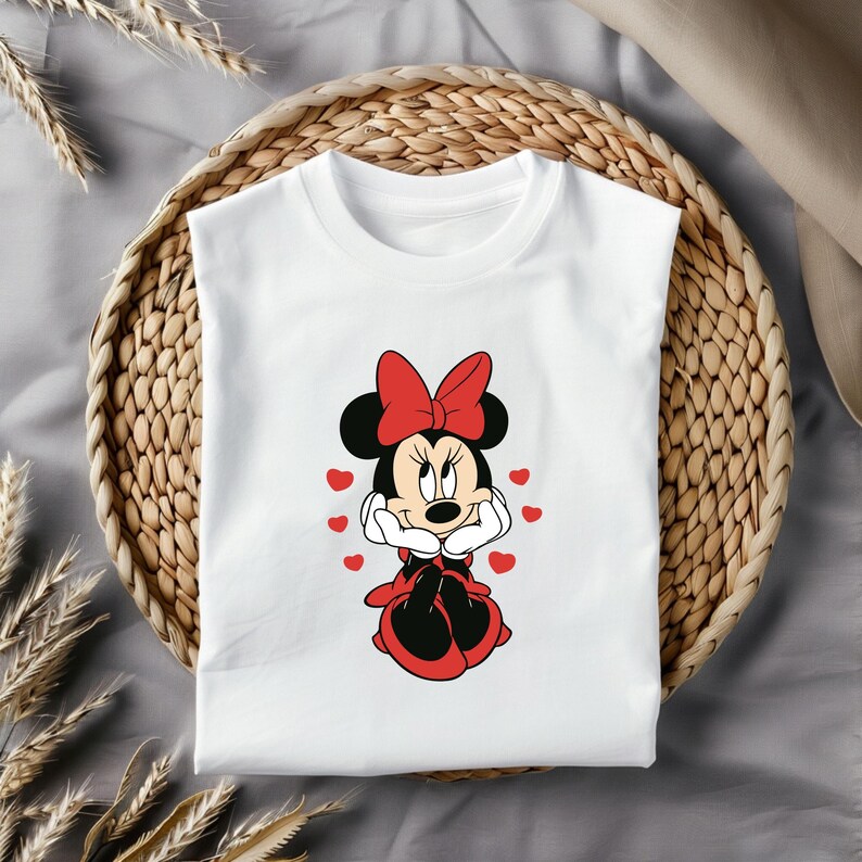 May include: White t-shirt with a red and black cartoon image of Minnie Mouse. Minnie Mouse is wearing a red dress and a red bow. She is surrounded by red hearts.