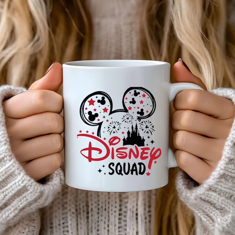 Pu&ograve; includere: Una tazza in ceramica bianca con un design nero e rosso che presenta le orecchie di Topolino, fuochi d'artificio e un'immagine stilizzata del castello di Cenerentola. Il testo "Disney Squad" &egrave; stampato in rosso e nero.