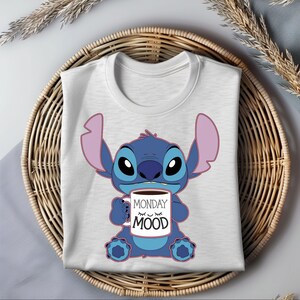 Puede incluir: Una camiseta blanca con un personaje azul Stitch sosteniendo una taza de caf&eacute; que dice "Monday Mood".