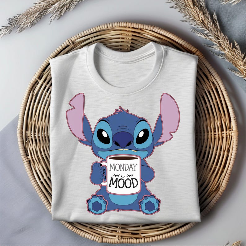 Puede incluir: Una camiseta blanca con un personaje azul Stitch sosteniendo una taza de caf&eacute; que dice "Monday Mood".