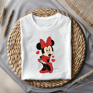 May include: White t-shirt with a red and black cartoon image of Minnie Mouse wearing a red dress and red shoes.  She has a red bow in her hair and is surrounded by red hearts.