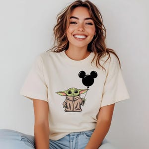 K&ouml;nnte beinhalten: Ein wei&szlig;es T-Shirt mit einer gr&uuml;nen Comicfigur, die einen schwarzen Mickey-Maus-Ballon h&auml;lt.
