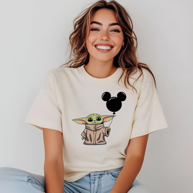 K&ouml;nnte beinhalten: Ein wei&szlig;es T-Shirt mit einer gr&uuml;nen Comicfigur, die einen schwarzen Mickey-Maus-Ballon h&auml;lt.