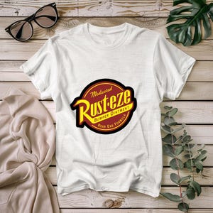 May include: White t-shirt featuring a red and yellow logo that reads "Medicated Rust-eze Bumper Ointment Rear End Formula".