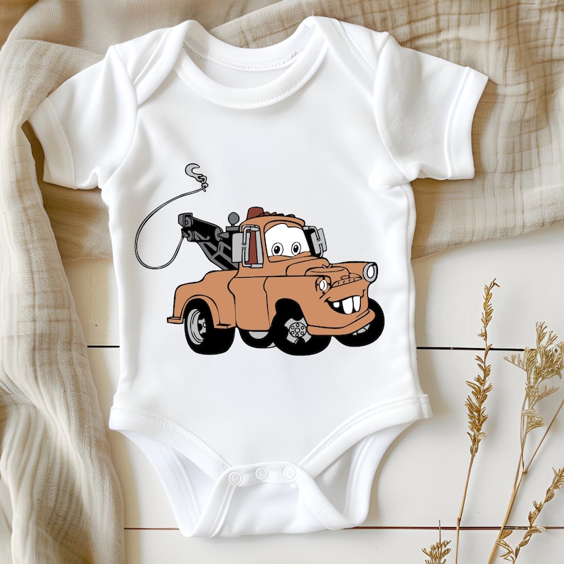 May include: White baby onesie featuring a cartoon image of Mater, the orange tow truck from the Disney Pixar film Cars. Mater is smiling and has a hook attached to his tow truck.