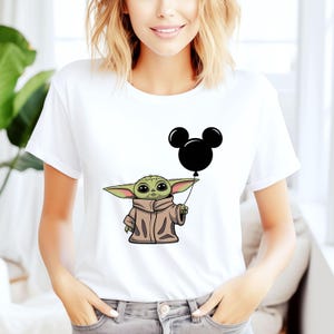 K&ouml;nnte beinhalten: Wei&szlig;es T-Shirt mit einer gr&uuml;nen Alienfigur, die einen schwarzen Mickey-Maus-Ballon h&auml;lt.