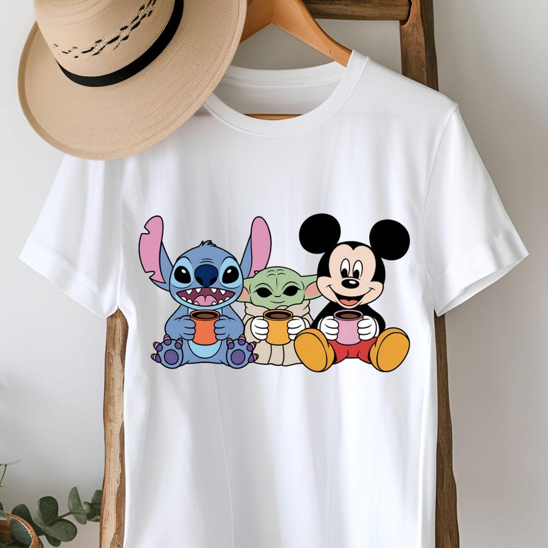 Puede incluir: Camiseta blanca con un gr&aacute;fico de Stitch, Baby Yoda y Mickey Mouse sosteniendo tazas de caf&eacute;.
