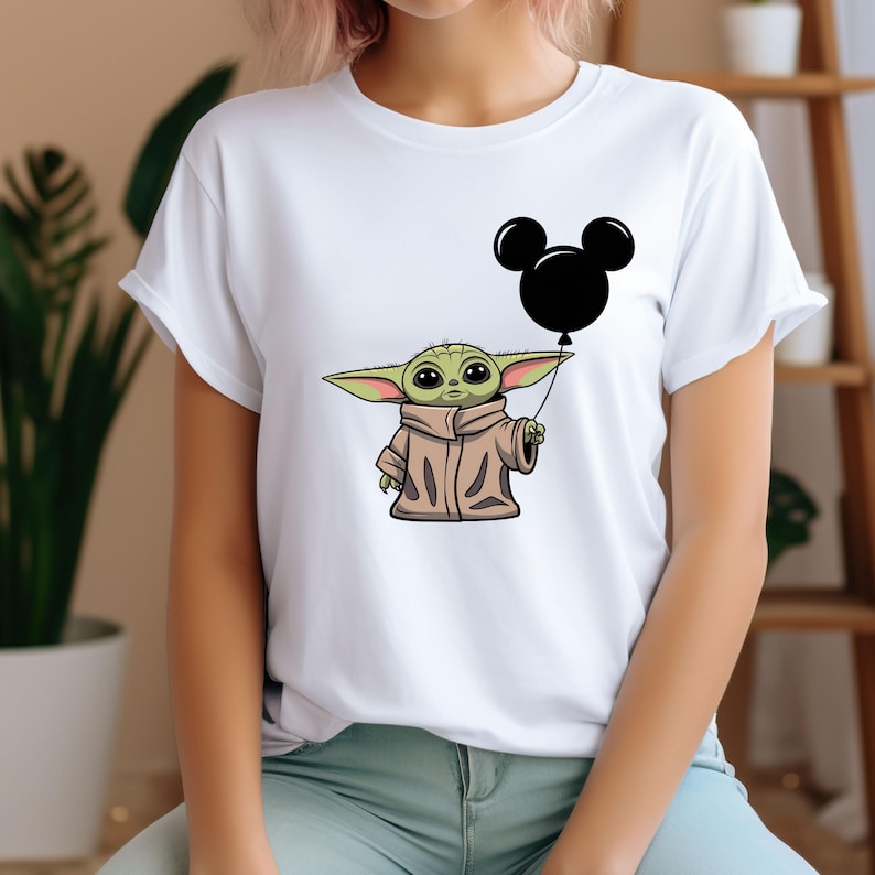 K&ouml;nnte beinhalten: Ein wei&szlig;es T-Shirt mit einer gr&uuml;nen Comicfigur, die einen schwarzen Mickey-Maus-Ballon h&auml;lt.